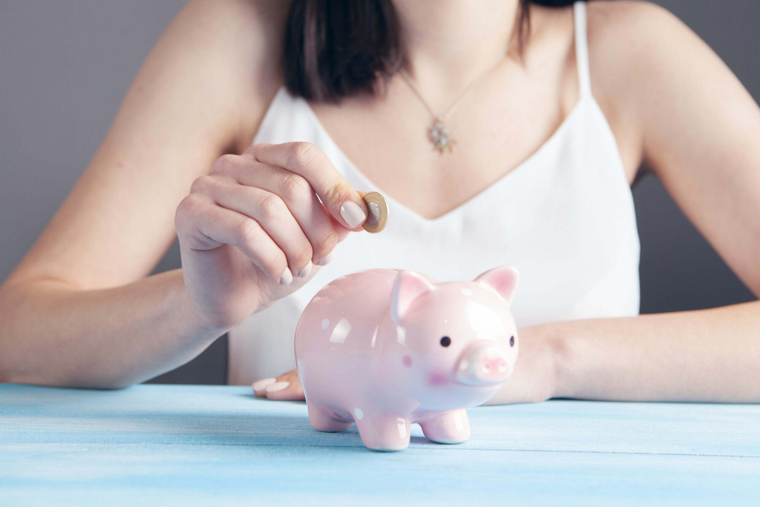 Person placing coin into pink piggy bank.